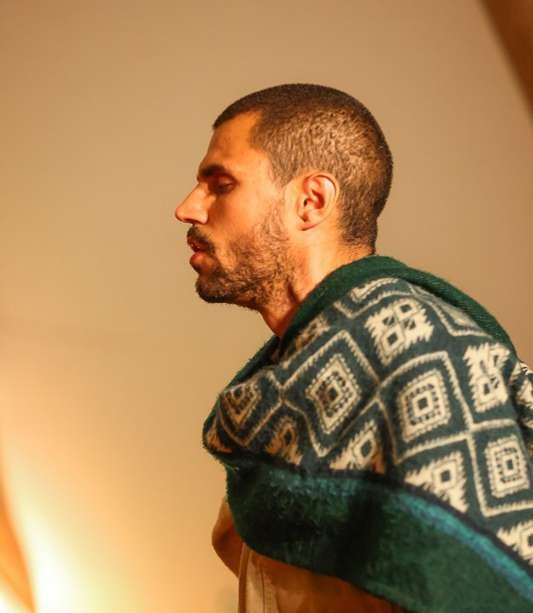 Homem de perfil, em silêncio, com um poncho de losangos verdes