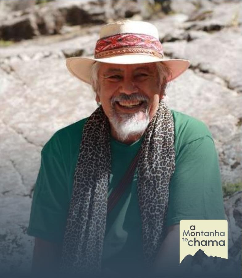 Suryavan Solar sorrindo, de chapéu e lenço, sobre rochas